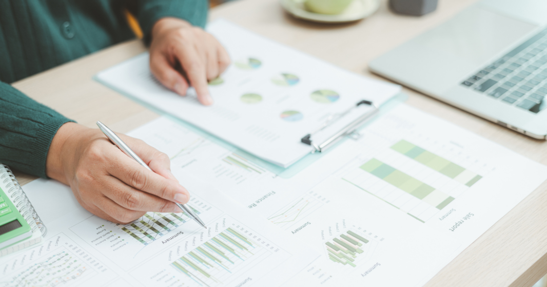 Analyst reviewing ecommerce performance charts and growth metrics on printed reports beside a laptop.