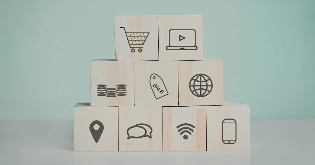 Wooden blocks stacked in a pyramid displaying ecommerce and digital marketing icons including shopping cart, sale tag, globe, mobile phone, chat, location, and Wi-Fi symbols representing online retail systems.