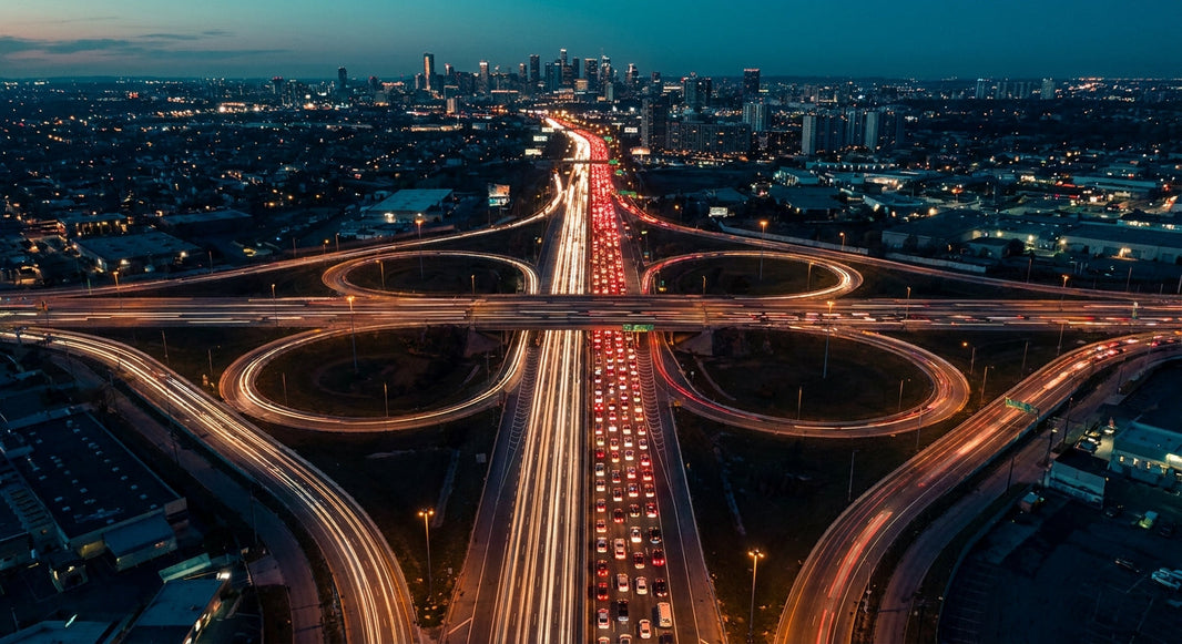 Aerial view of a congested highway interchange leading into a city skyline, illustrating complex traffic flow and bottlenecks.