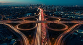 Aerial view of a congested highway interchange leading into a city skyline, illustrating complex traffic flow and bottlenecks.