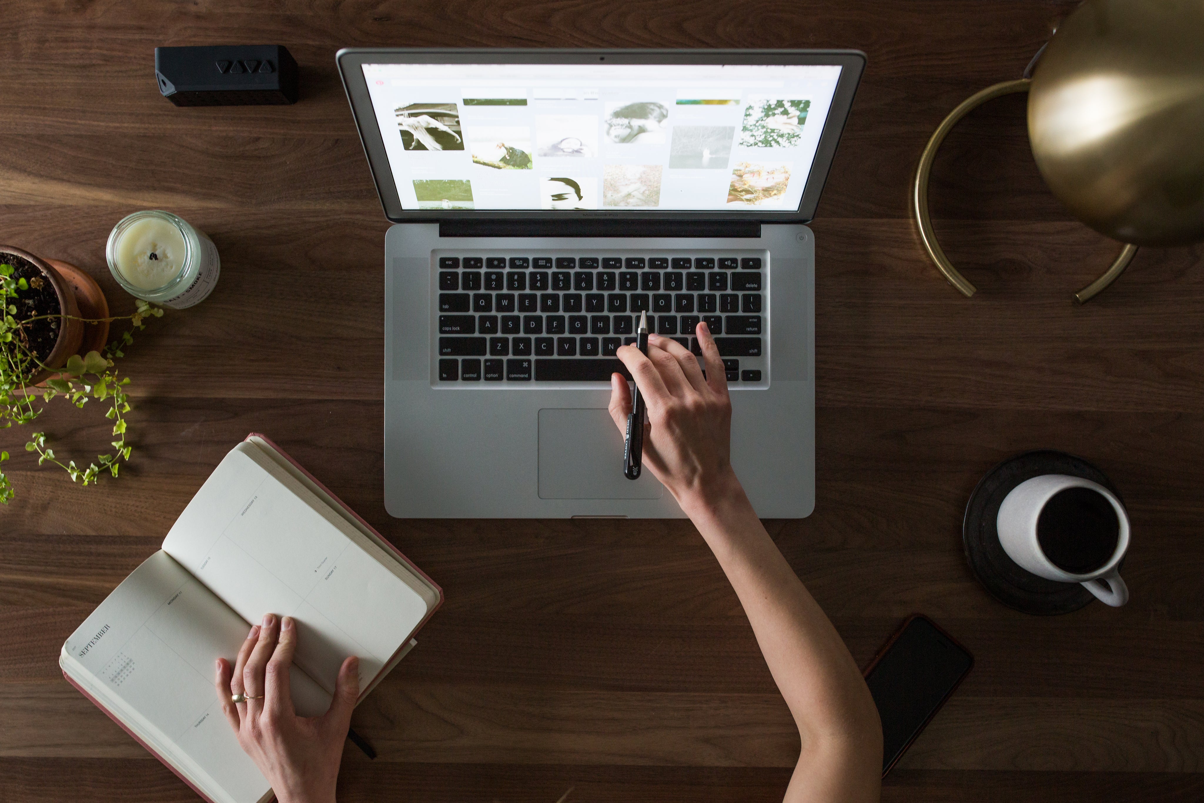 Person using a laptop on a wooden desk with a notebook and coffee cup.