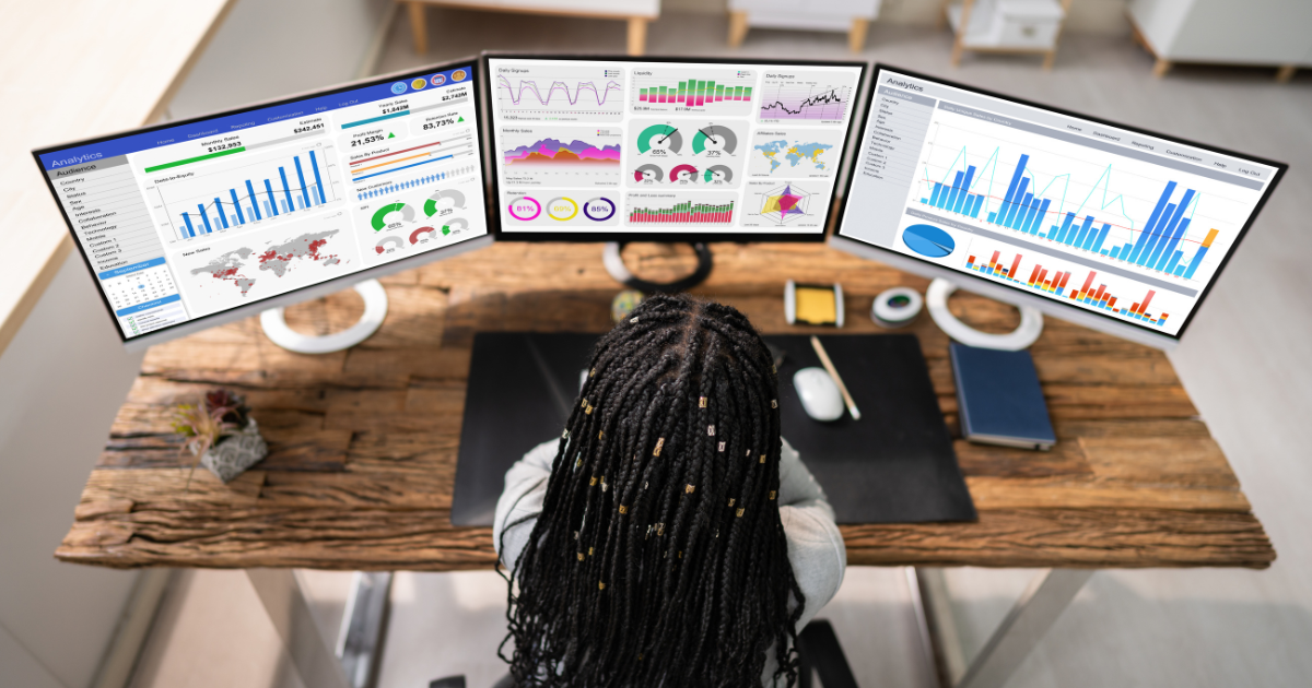 Marketing professional reviewing performance dashboards across three computer monitors.